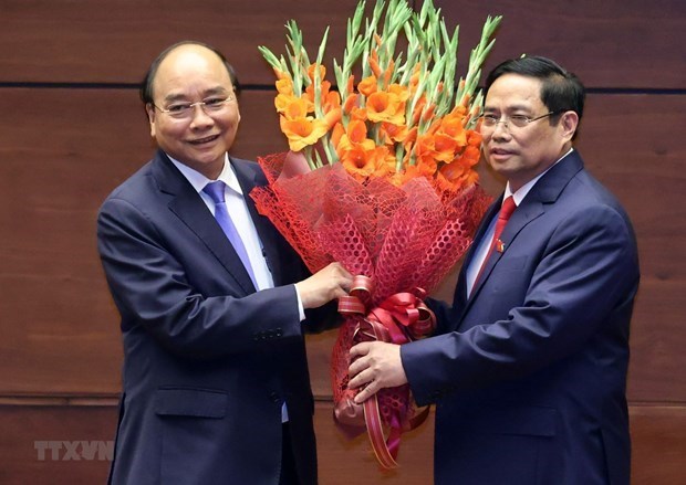 Prime Minister Pham Minh Chinh (R) presents flowers to State President Nguyen Xuan Phuc, who is the Prime Minister in the 2016-2021 tenure (Photo: VNA)